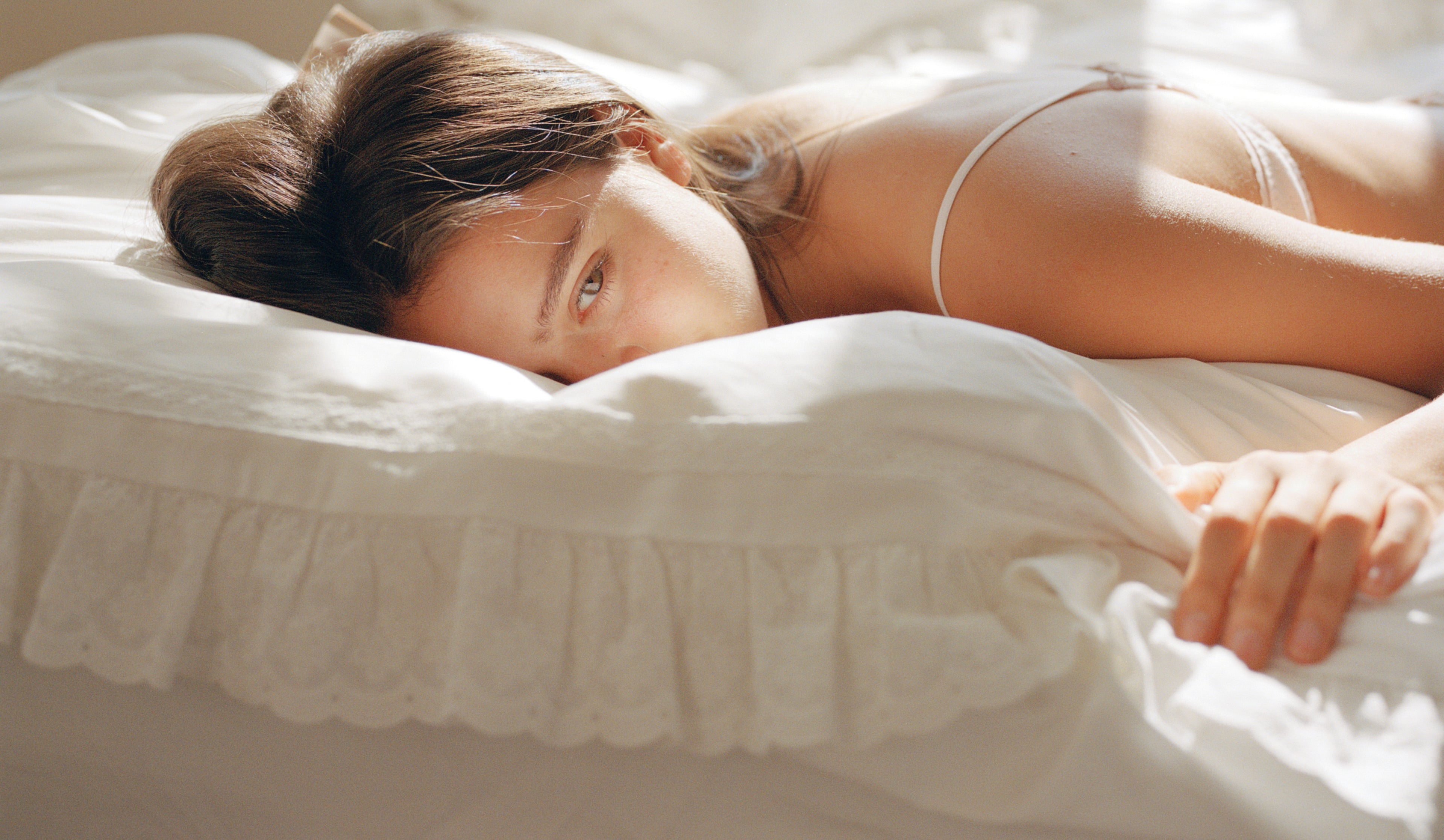 Model resting on Laiterie Chantilly duvet cover with soft white cotton and eyelet ruffle trim