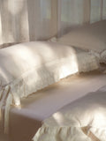 Chantilly ruffle and bow pillowcase in ivory Egyptian cotton sateen on a sunlit bed