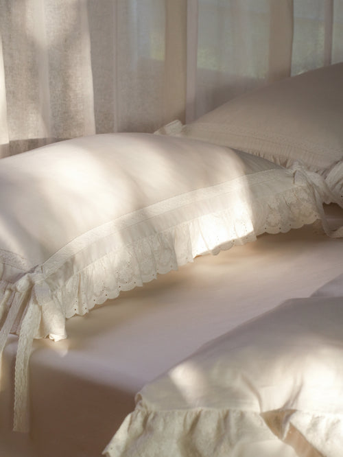 Chantilly ruffle and bow pillowcase in ivory Egyptian cotton sateen on a sunlit bed