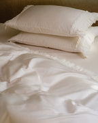 Stacked Crème ruffle pillowcases in ivory Egyptian cotton sateen on a styled bed