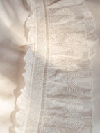 Close-up of embroidered scalloped ruffles and airy gauze detailing from the Crème Collection