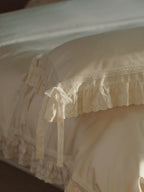 Chantilly ruffle pillowcase with scalloped eyelet detailing styled on an ivory bed